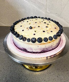 A cheesecake ringed with fresh blueberries on a silver cake stand.