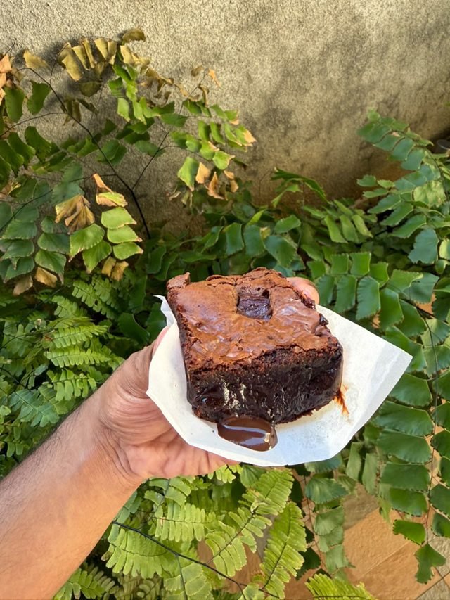 A thick fudge brownie on parchment with molten chocolate running from its centre.