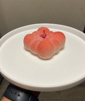 A peach-shaped mousse dessert with a soft coral finish, on white porcelain.