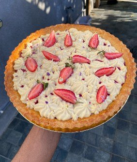 A golden tart shell filled with piped cream and laid with strawberry halves.